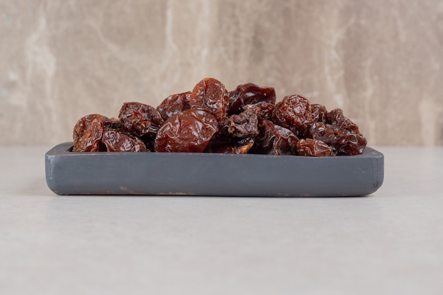 Brown dried cherries on a wooden platter.