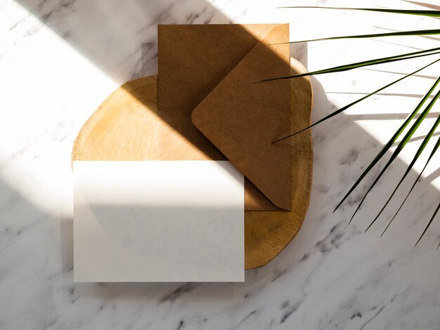 Brown envelope with a white blank on a wooden plate on a marble background with green leafs