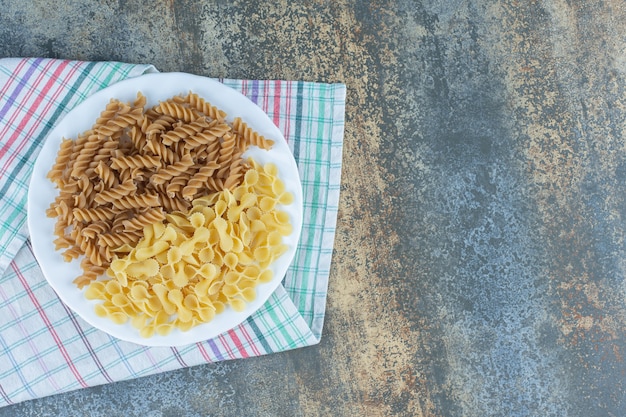 Free Photo brown fusilli pasta and farfalle pastas in the bowl on the towel, on the marble surface. 