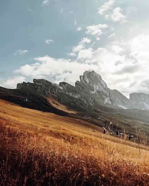 Brown grass field near mountains under white clouds during daytime