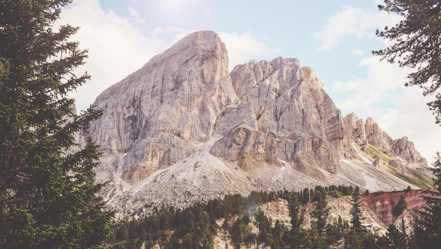 Brown mountain near green trees under white and blue sunny cloudy sky