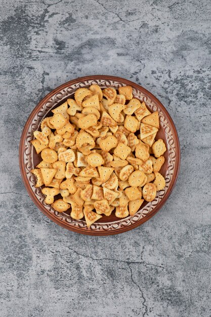 Brown plate full of dry salted crackers on marble background.