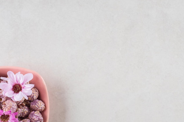 Brown popcorn candy and flowers in a pink bowl on marble table.