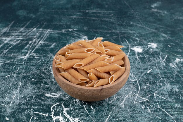 Brown raw penne pasta in wooden bowl. High quality photo