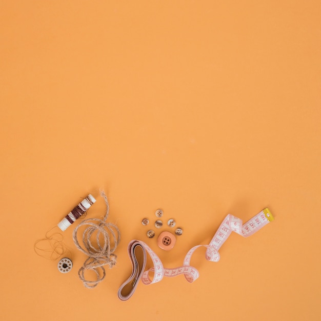 Brown spool; string; buttons and measuring tape on an orange backdrop