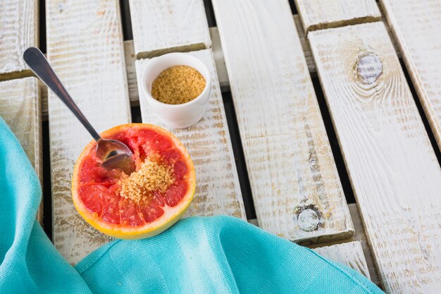 Brown sugar and spoon on halved grapefruit with napkin on wooden backdrop