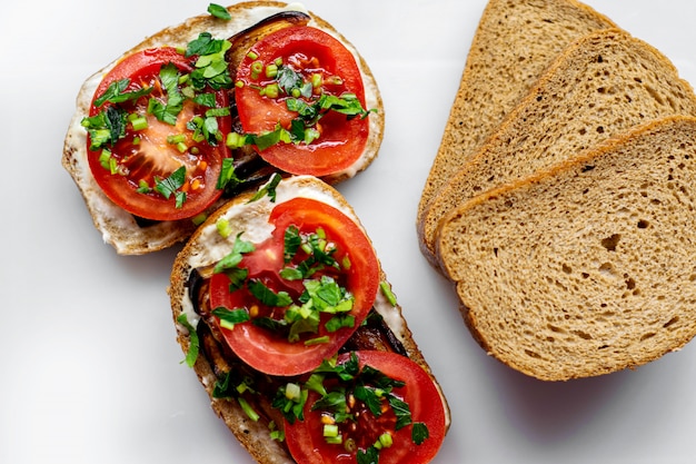 Brown toasts hot bread slices along with red sliced tomatoes and fried black eggplant with greens on white floor