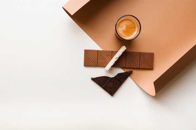 Free photo brown; white and dark chocolate bar with coffee glass on paper against white backdrop