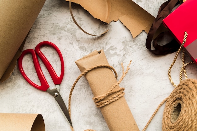 Free photo brown wrapped gift box with string and scissor on white textured background