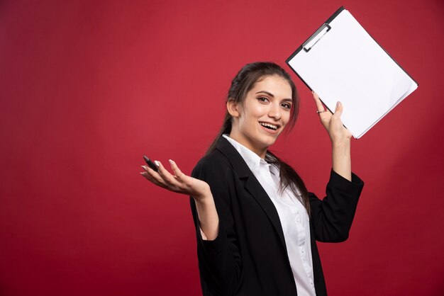 Brunette businesswoman posing with clipboard on red background. 