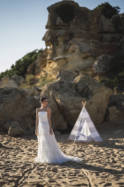 Free Photo brunette caucasian bride posing at the beach in front of a white tent