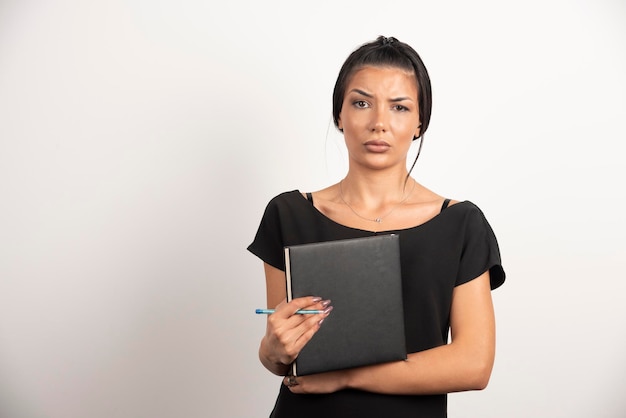 Brunette employee with notebook posing on white wall.