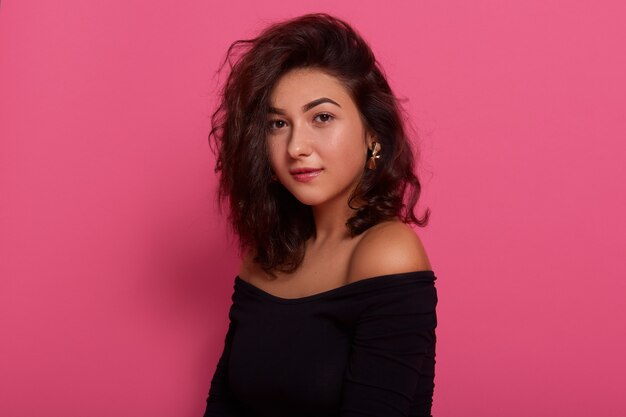 Brunette female posing with bare shoulders against pink wall,