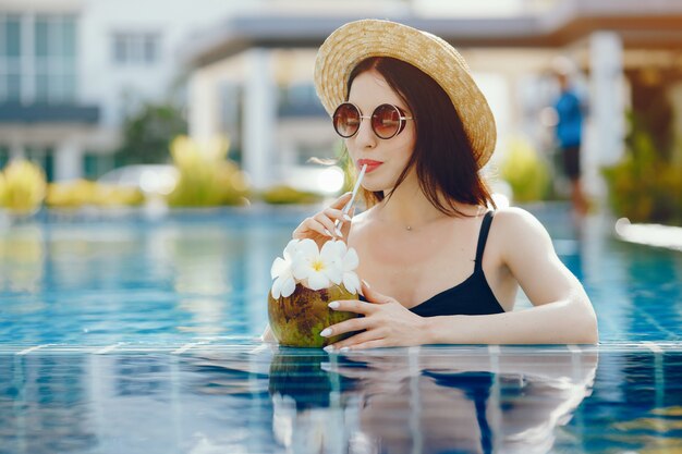 brunette girl drinking coconut juice by the pool