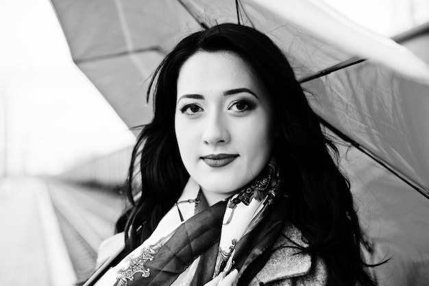 Brunette girl in gray coat with red umbrella in railway station