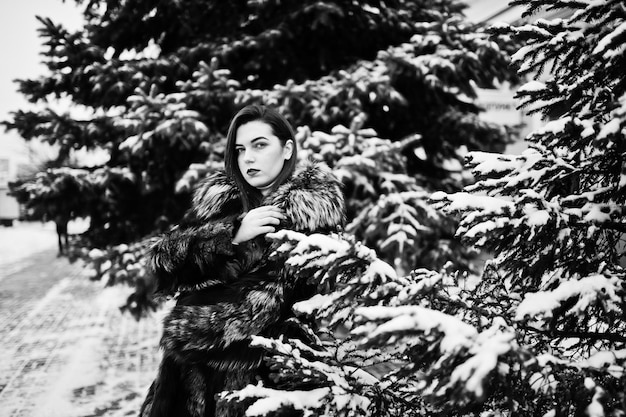 Brunette girl in green fur coat at winter day against snowy pine tree