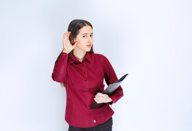 A brunette girl model standing and posing with a folder against white wall.