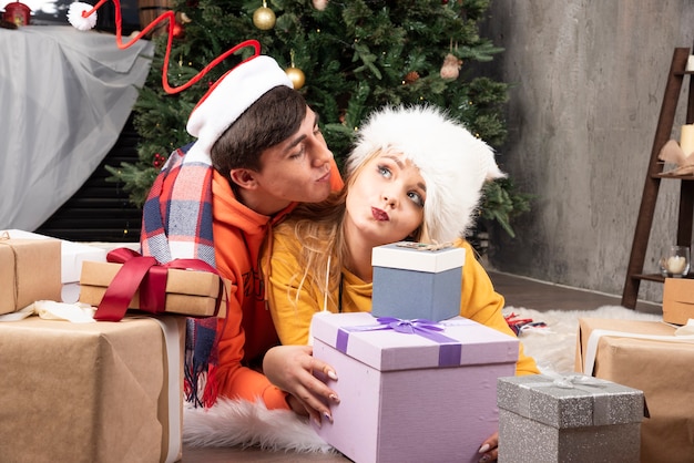 Brunette guy kissing on cheek blonde woman in Christmas hat