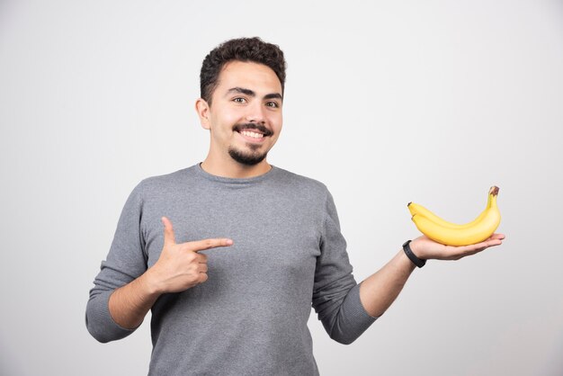 Brunette male pointing at banana on gray.