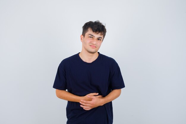 Brunette man holding hands on stomach in dark t-shirt and looking painful , front view.