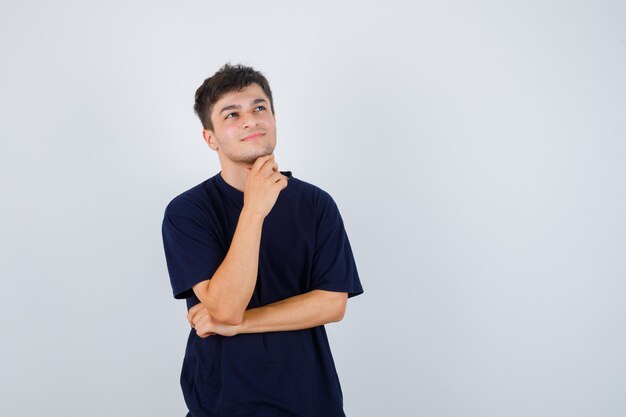 Brunette man in t-shirt holding hand under chin and looking thoughtful , front view.