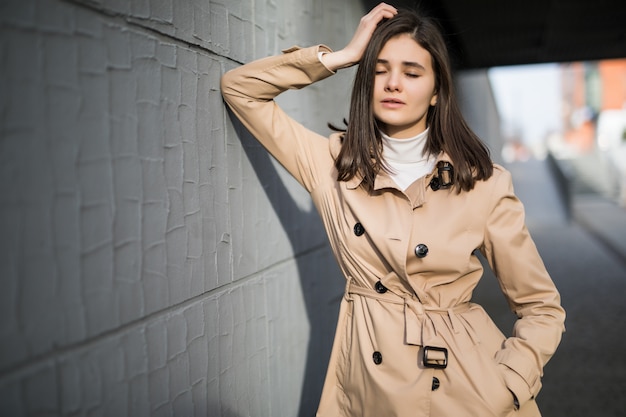 Free photo brunette model with clothed eyes stays near grey wall outside