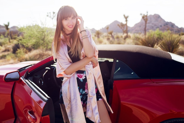 Brunette pretty seductive girl  posing near  red modern sport convertible car. 