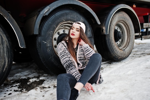 Brunette stylish casual girl in cap sitting against truck wheels