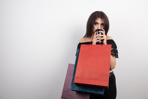 Brunette woman carrying shopping bags and coffee cup.