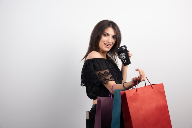 Brunette woman holding shopping bags and coffee cup.