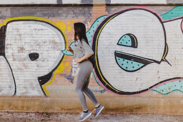 Free photo brunette woman running against concrete wall