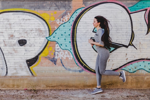 Free photo brunette woman running against concrete wall