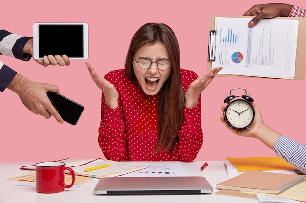 Free photo brunette woman sitting at desk surrounded with gadgets and papers