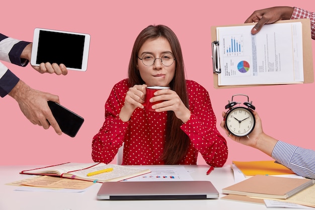 Free photo brunette woman sitting at desk surrounded with gadgets and papers