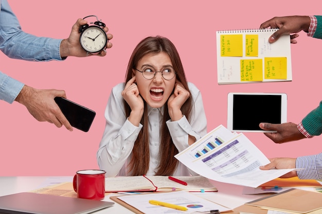 Free photo brunette woman sitting at desk surrounded with gadgets and papers