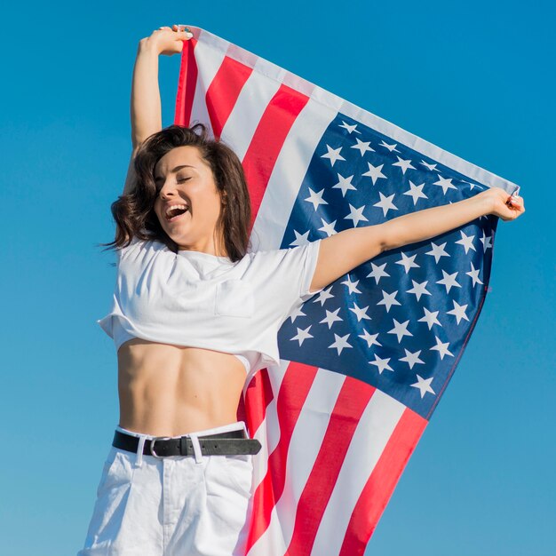 Brunette woman in white clothes holding big usa flag