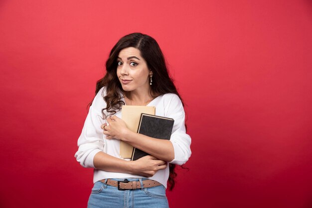 Brunette woman with books standing on red background. High quality photo