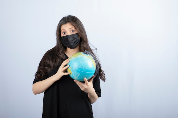 Free photo brunette woman with long hair in medical mask holding world globe .