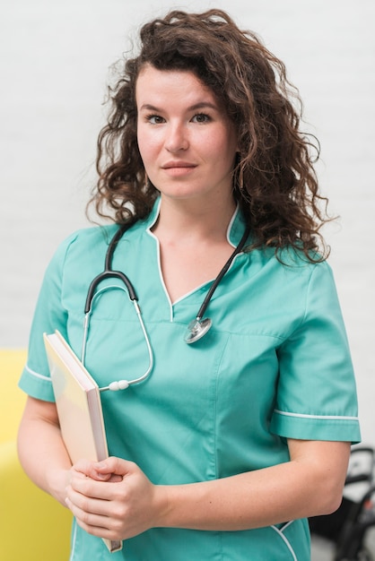 Free photo brunette young female nurse holding book and stethoscope around her neck