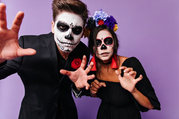 Brunette young people making funny faces during halloween photoshoot. Refined friends having fun at party in zombie costumes.