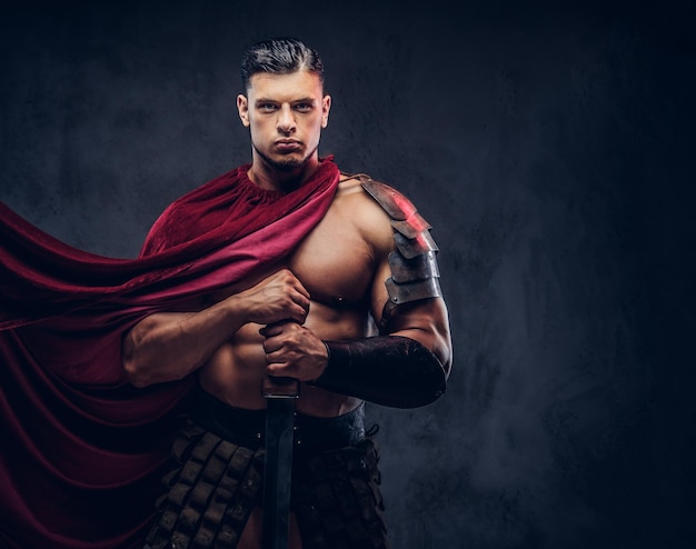 Free photo brutal ancient greece warrior with a muscular body in battle uniforms posing on a dark background.