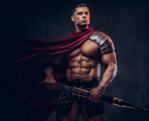 Free photo brutal ancient greece warrior with a muscular body in battle uniforms posing on a dark background.