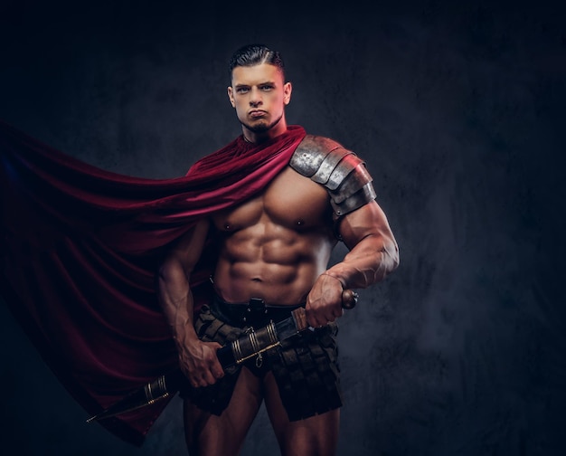 Free photo brutal ancient greece warrior with a muscular body in battle uniforms posing on a dark background.