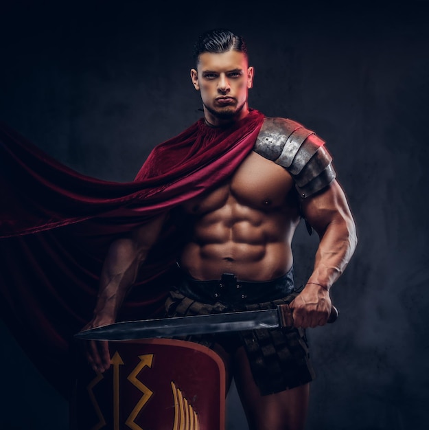 Free photo brutal ancient greece warrior with a muscular body in battle uniforms posing on a dark background.