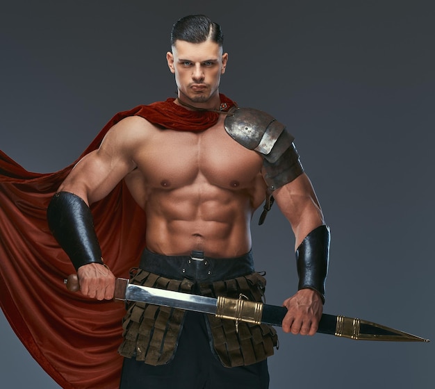 Brutal ancient Greece warrior with a muscular body in battle uniforms posing on a gray background.