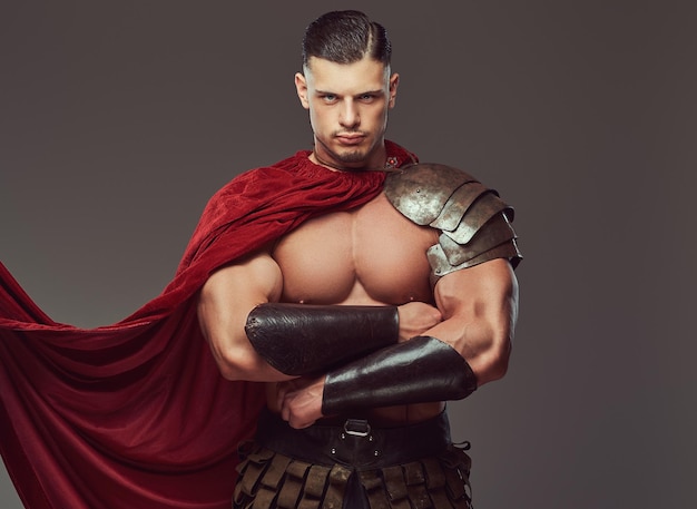 Free photo brutal ancient greece warrior with a muscular body in battle uniforms standing with crossed arms. isolated on a gray background.