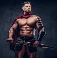 Free photo brutal ancient greek warrior with a muscular body in battle equipment posing on a dark background.