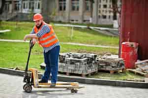 Free photo brutal beard worker man suit construction worker in safety orange helmet with pallet truck