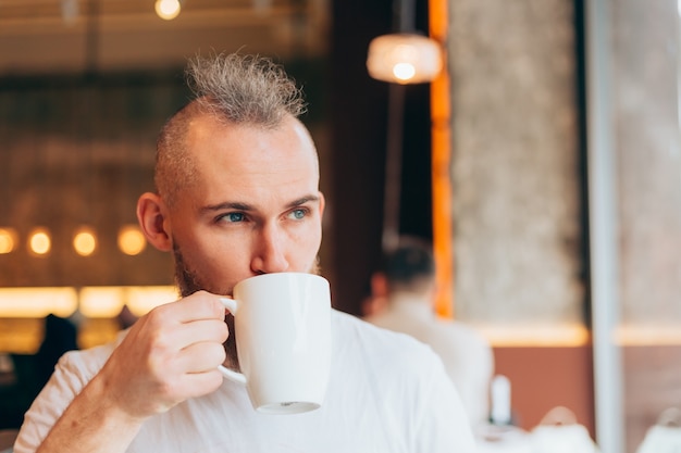 Brutal man of European appearance in a cafe in the morning with a cup of hot coffee