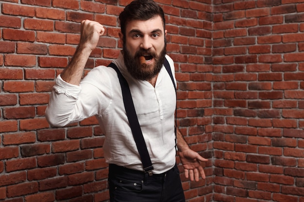 Brutal rage young handsome man smoking cigar on brick wall.